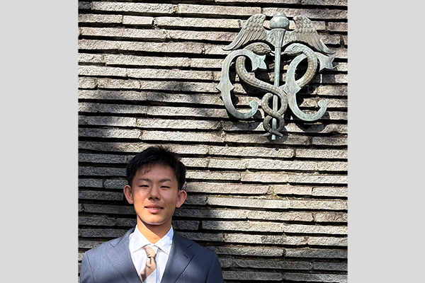 校章を背景に記念撮影を行う福井さん