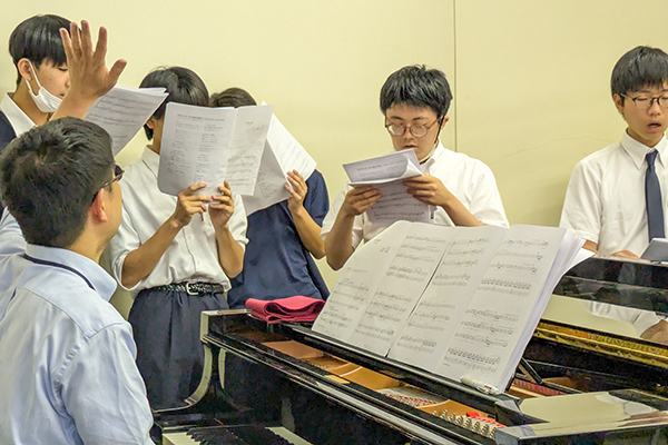 音楽室で楽譜を手に合唱練習をする生徒たち