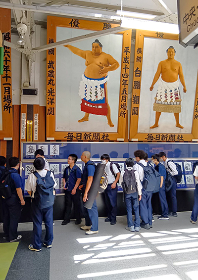 両国駅の構内で、壁に掲げられた歴代横綱の大きな肖像画を見上げる生徒たち