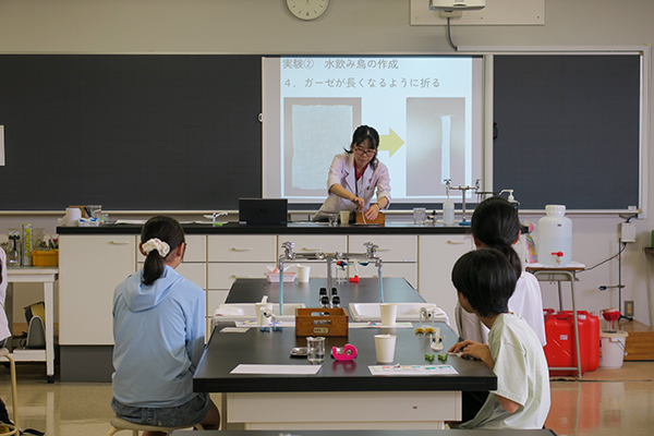 理科の体験企画「水飲み鳥を作ろう!」で実演する先生と真剣に見入る参加者