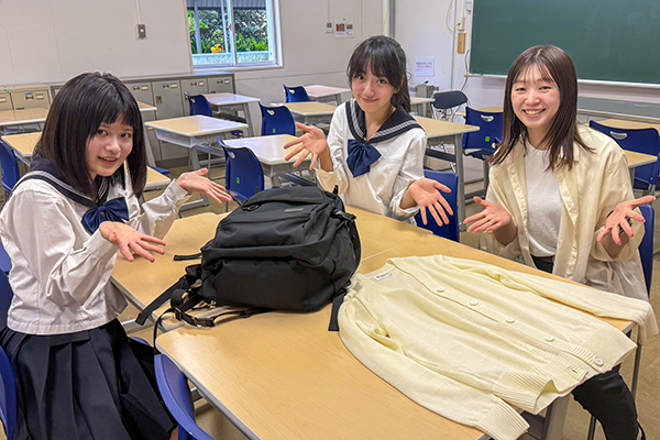 先生と生徒の前に、学校制定品のバッグとカーディガンが置かれている