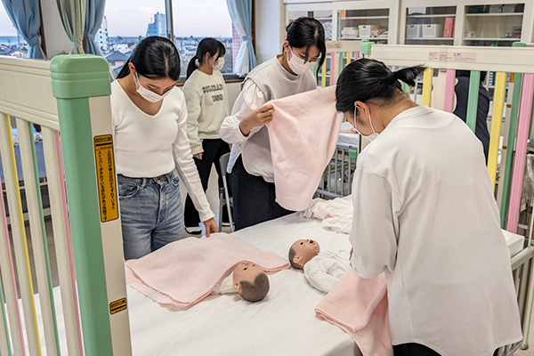 亀田医療大学訪問プログラムの様子。乳児の実習モデルを使った対応を学ぶ生徒たち。