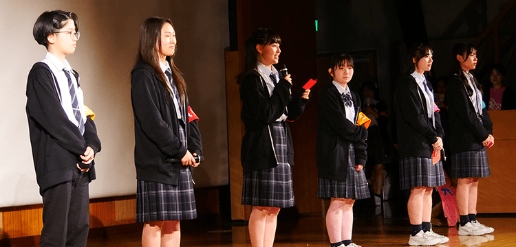 文化祭の会場にて挨拶するR.H.さんと委員会メンバーの写真