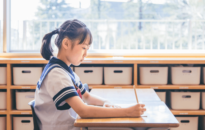教室の机に座って勉強している女子児童
