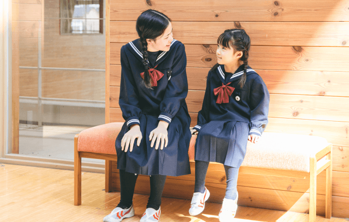 ベンチに座っている上級生と下級生の女子児童が話をしている様子